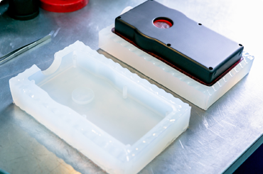 White silicone mold beside a black enclosure casting on a workbench
